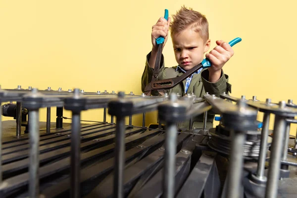 Ser allvarligt ut. Liten pojke, barn i bild av auto mekaniker eller montör i fängelsehålor med arbetsverktyg reparera auto motor isolerad på gul bakgrund. — Stockfoto