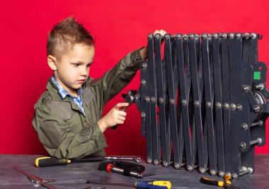 Küçük işçi. Sevimli anaokulu çocuğu, araba tamircisi görünümündeki çocuk ya da iş aletleriyle kırmızı arka planda izole edilmiş iş aletleri ile uyumlu..