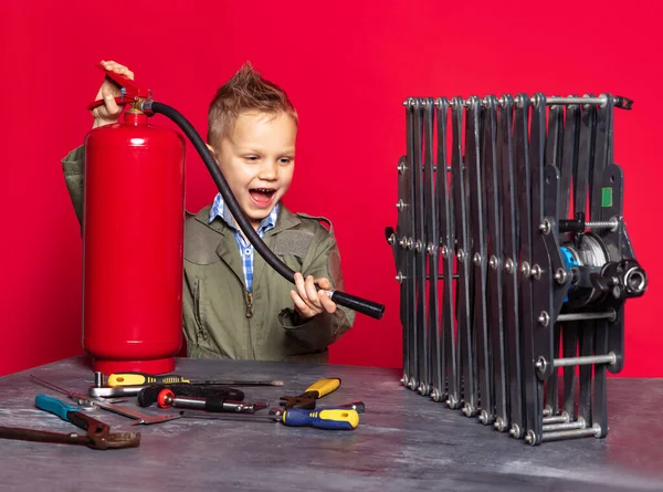 Pequena trabalhadora. Menino pré-escolar bonito, criança na imagem de mecânico de automóveis ou montador em dungarees com ferramentas de trabalho reparando isolado no fundo vermelho. — Fotografia de Stock