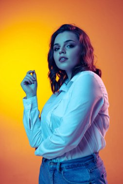 Uzun kıvırcık saçlı güzel bir kızın portresi turuncu arka planda izole edilmiş, neon ışıklı, filtreli. Duygular, güzellik, moda kavramı