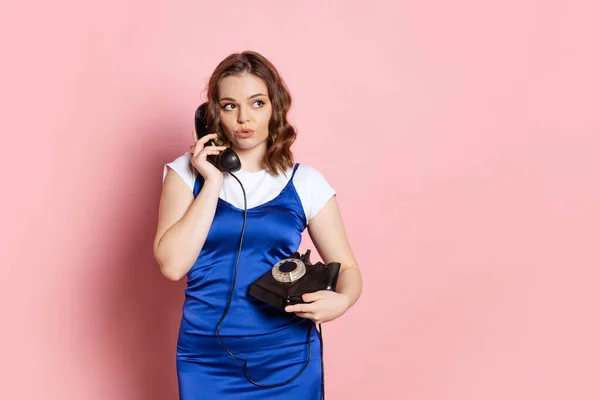 Πορτρέτο της νεαρής κοπέλας φορώντας ρετρό στυλ ενδυμασία χρησιμοποιώντας vintage τηλέφωνο απομονώνονται σε ροζ φόντο. Έννοια των συναισθημάτων, ομορφιά, μόδα, σύγκριση εποχών — Φωτογραφία Αρχείου