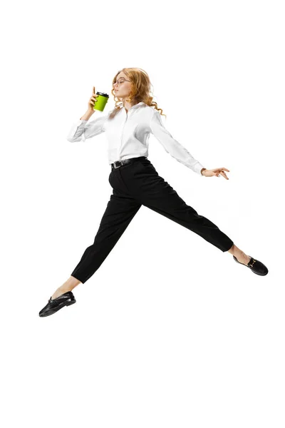 Retrato dinámico de una joven bonita con ropa de negocios saltando con café aislado sobre fondo blanco. Finanzas, ballet, arte, negocios, concepto de belleza. — Foto de Stock