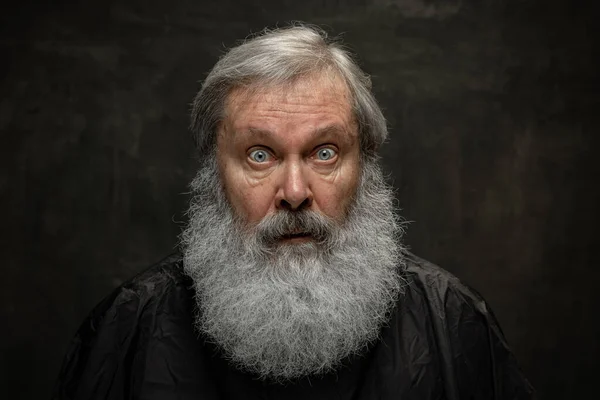 Dramatisches Porträt eines älteren, bärtigen Mannes, der sich auf dunklem Vintage-Hintergrund isoliert einen Bart pflegt. Konzept von Emotionen, Mode, Schönheit, Selbsterfindung — Stockfoto