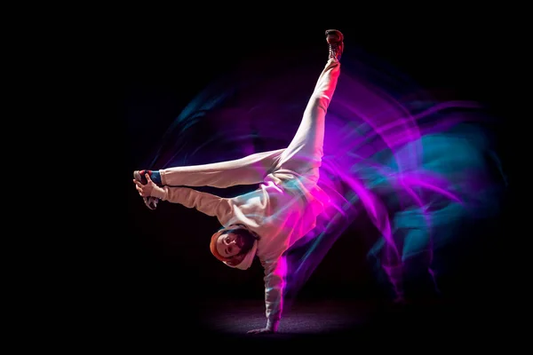 若い柔軟なスポーツ少年のダイナミックな肖像画混合ピンクのネオンの光の中で暗い背景に白い衣装でヒップホップやブレークダンスを踊る。スポーツ、アート、アクション、動き — ストック写真