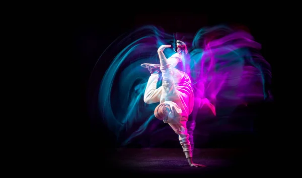 Динамичный портрет молодого гибкого спортивного мальчика, танцующего хип-хоп или брейк-данс в белом наряде на тёмном фоне в смешанном розовом неоновом свете. Спорт, искусство, действие, движения — стоковое фото
