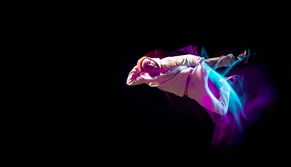Dynamický portrét mladého ohebného sportovního chlapce tancujícího hip-hop nebo breakdance v bílém oblečení na tmavém pozadí ve smíšeném růžovém neonovém světle. Sport, umění, akce, pohyby — Stock fotografie