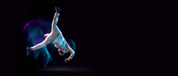 Подставка для рук. Один энергичный молодой гибкий спортивный человек танцует хип-хоп или брейк-данс в белом наряде на тёмном фоне в смешанном синем неоновом свете. Спорт, искусство, действие, движения — стоковое фото