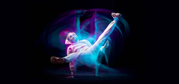 Un giovane uomo sportivo flessibile energia ballare hip-hop o breakdance in abito bianco su sfondo scuro in luce al neon blu misto. Sport, arte, azione, mosse — Foto Stock