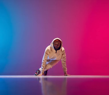 Genç, esnek, sporcu bir adamın gradyan pembe arka planda dans edişinin stüdyo çekimi. Eylem kavramı, sanat, güzellik, spor, gençlik