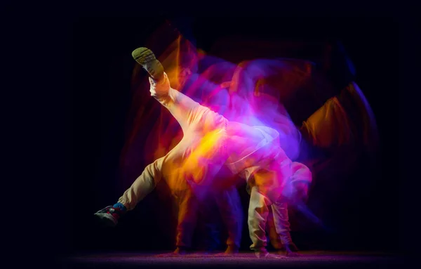 Solo dansen. Jonge flexibele sportieve man dansend hip-hop of breakdance in witte outfit op donkere achtergrond in gemengd geel neon licht. Schoonheid, sport, jeugd, actie, bewegingen — Stockfoto