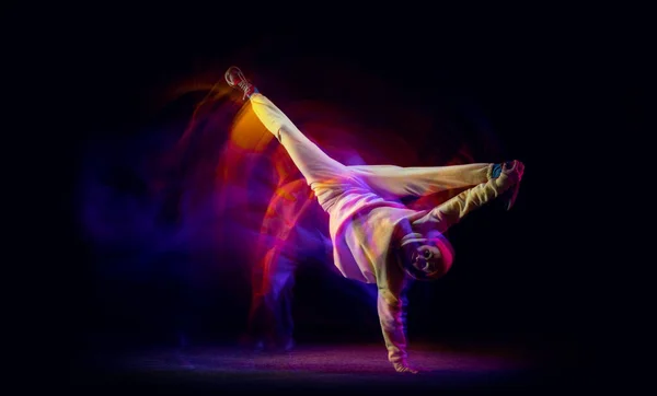 Сольный танец. Молодой гибкий спортивный мужчина танцует хип-хоп или брейк-данс в белом наряде на тёмном фоне в смешанном жёлтом неоновом свете. Красота, спорт, молодость, действие, движения — стоковое фото