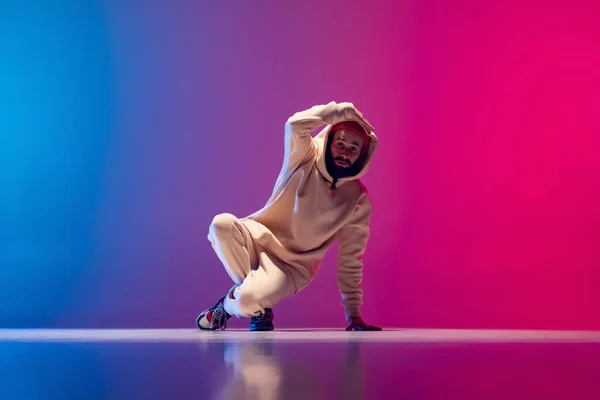 Estudio de un joven hombre deportivo flexible bailando breakdance en traje blanco sobre fondo azul rosado degradado. Concepto de acción, arte, belleza, deporte, juventud — Foto de Stock