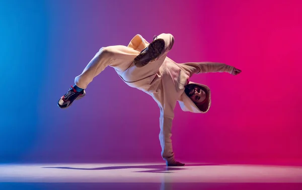 Estúdio tiro de jovem homem esportivo flexível dança breakdance em roupa branca em gradiente rosa fundo azul. Conceito de ação, arte, beleza, esporte, juventude — Fotografia de Stock