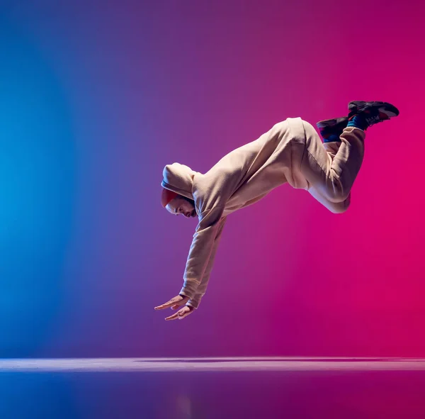 Queda livre. Estúdio tiro de jovem homem esportivo flexível dança breakdance em roupa branca em gradiente rosa fundo azul. Conceito de ação, arte, beleza, esporte, juventude — Fotografia de Stock