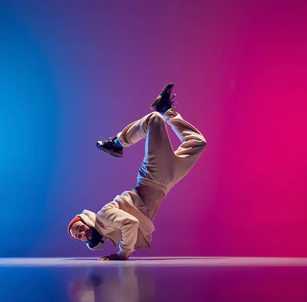 Free fall. Studio shot of young flexible sportive man dancing breakdance in white outfit on gradient pink blue background. Concept of action, art, beauty, sport, youth — Stock Photo, Image