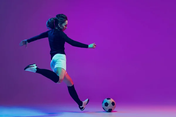 Futbol topuyla antrenman yapan bayan futbolcunun dinamik portresi neon ışıklarıyla izole edilmiş mor stüdyo arka planında. Spor, eylem, hareket, fitness — Stok fotoğraf