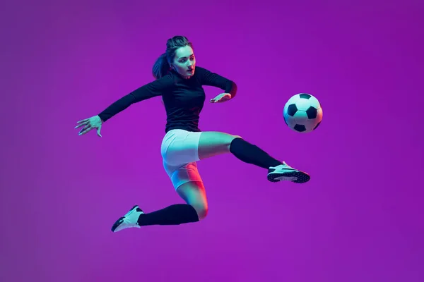 One sportive girl, female soccer player kick in jump football ball isolated on purple studio background in neon light. Sport, action, motion, fitness — Stock Photo, Image