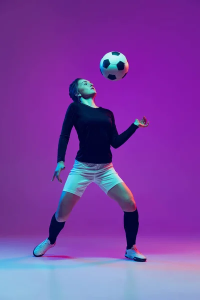 Emotive girl, female soccer, football player in motion, action isolated on purple studio background in neon light. Sport, active, healthy lifestyle — Stock Photo, Image