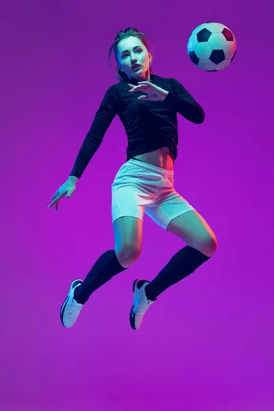 In action. One sportive girl, female soccer player training with football ball isolated on purple studio background in neon light. Sport, action, motion, fitness — Stock Photo, Image