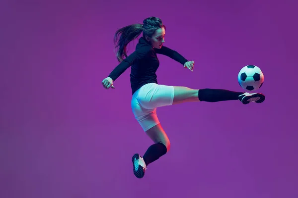 In Aktion. Ein sportliches Mädchen, weibliche Fußballspielerin beim Training mit Fußballball isoliert auf lila Studiohintergrund in Neonlicht. Sport, Action, Bewegung, Fitness — Stockfoto