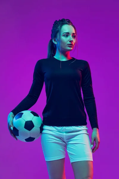 Ritratto di bella ragazza, calciatrice professionista in posa con pallone da calcio isolato su sfondo viola studio in luce al neon. Sport, squadra, giochi, fitness — Foto Stock