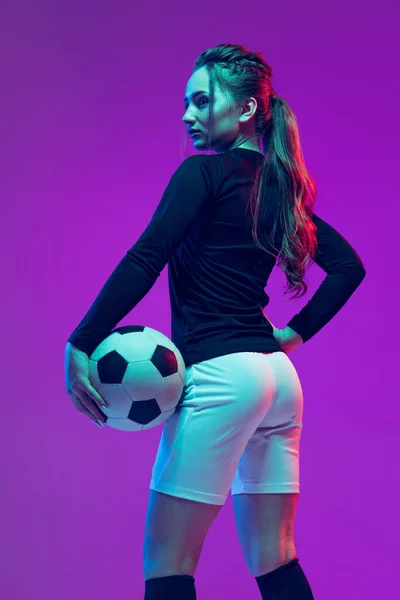 Güzel bir kızın portresi, profesyonel bayan futbolcu futbol topuyla poz veren neon ışıklarıyla izole edilmiş mor stüdyo arka planında. Spor, takım, oyunlar, fitness — Stok fotoğraf