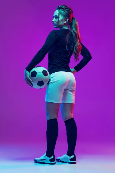 漂亮女孩的肖像，专业的女足球运动员在霓虹灯下与紫色工作室背景隔离的足球合影。体育、团队、游戏、健身 — 图库照片