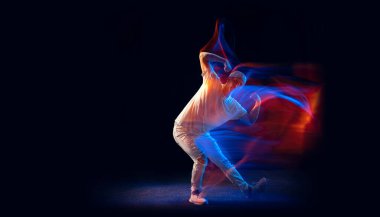 Sportif beyaz takım elbiseli, hip-hop dansçısı, koyu bir arka planda, karışık neon ışıkta izole edilmiş. Gençlik kültürü, hip-hop, hareket, tarz ve moda, aksiyon.