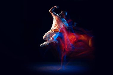 Atlıyorum. Beyaz spor kıyafetli şık bir adam hip-hop yapıyor, breakdance karanlık arka planda karışık neon ışıkta izole edilmiş. Gençlik kültürü, hip-hop, tarz ve moda, aksiyon.