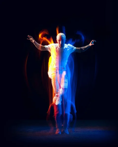 Portrét muže v bílém sportovním obleku, hip-hopová tanečnice letící izolovaně na tmavém pozadí ve smíšeném neonovém světle. Mládež kultura, hip-hop, pohyb, styl a móda, akce. — Stock fotografie