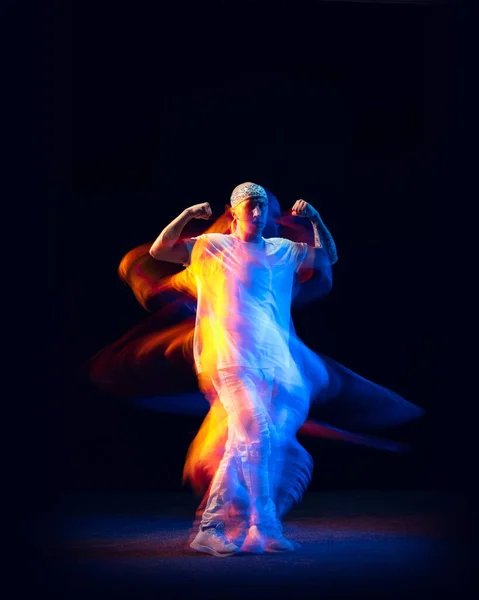 Спортивный человек в спортивном белом костюме танцующий хип-хоп изолирован на тёмном фоне в смешанном неоновом свете. Молодежная культура, хип-хоп, движение, стиль и мода, экшн. — стоковое фото