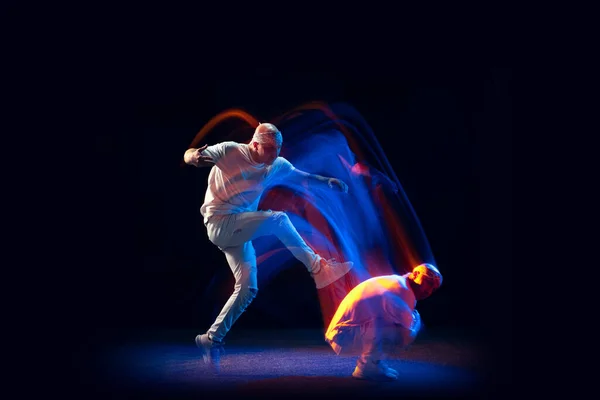 Rozdělená osobnost. Sportovní muž ve sportovní bílé uniformě a do-hadr tanec hip-hop izolované na tmavém pozadí ve smíšeném neonovém světle. Mládež kultura, styl a móda — Stock fotografie