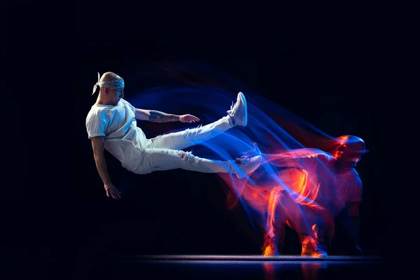 Gesplitste persoonlijkheid. Sportieve man in sportief wit uniform en do-vod dansende hiphop geïsoleerd op donkere achtergrond in gemengd neonlicht. Jeugdcultuur, stijl en mode — Stockfoto