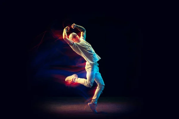 Vrijheid. Flexibele man in witte jeans en tee dancing hip-hop geïsoleerd op donkere achtergrond in gemengd neon licht. Jeugdcultuur, straatstijl en mode, actie. — Stockfoto