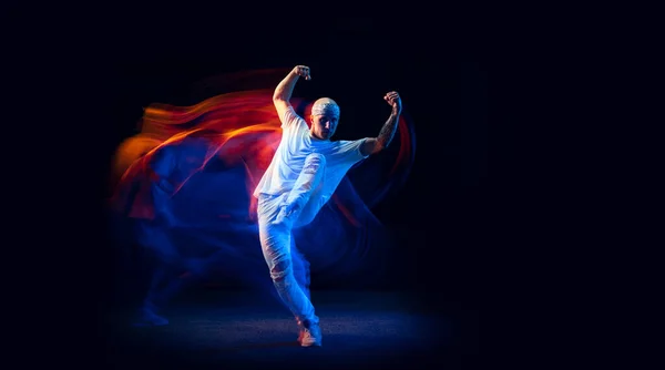 Personalidade dividida. Homem esportivo de uniforme branco esportivo e do-rag dançando hip-hop isolado em fundo escuro em luz de néon misto. Cultura, estilo e moda juvenis — Fotografia de Stock