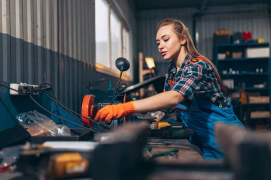 Kadın otomobil tamircisi. Güzel, kızıl saçlı bir kız, otomobil istasyonunda çalışıyor, kapalı bir yerde. Cinsiyet eşitliği. İş, meslek, moda, iş
