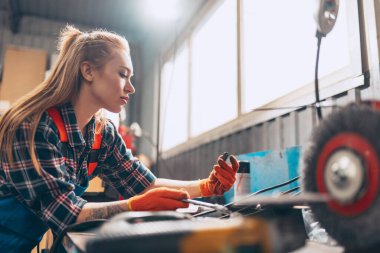 Kadın otomobil tamircisi. Güzel, kızıl saçlı bir kız, otomobil istasyonunda çalışıyor, kapalı bir yerde. Cinsiyet eşitliği. İş, meslek, moda, iş