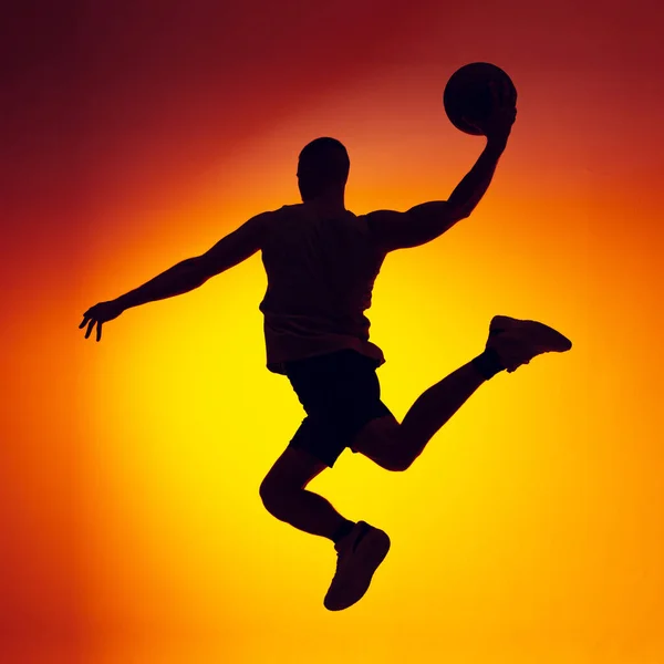 Silhouette eines Basketballspielers in Bewegung, Aktion isoliert auf einem Gefälle gelb-orangefarbenen Hintergrund in Neonlicht. Sport, Vielfalt, Aktivitätskonzepte. — Stockfoto