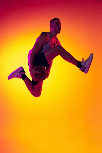 Уличный футболист. Мужчина баскетболист, спортсмен прыгающий с мячом изолированным на градиентном желтом оранжевом фоне в неоновом свете. Спорт, разнообразие, концепции деятельности. — стоковое фото