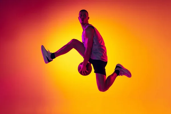 Streetballer. Man basketbalspeler, atleet springen met bal geïsoleerd op gradiënt geel oranje achtergrond in neon licht. Sport, diversiteit, activiteitsconcepten. — Stockfoto