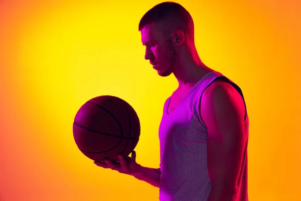Studio shot van gespierde man, basketbalspeler, danker geïsoleerd op gradiënt geel paarse achtergrond in neon licht. Schoonheid, sport, beweging, activiteitsconcepten. — Stockfoto