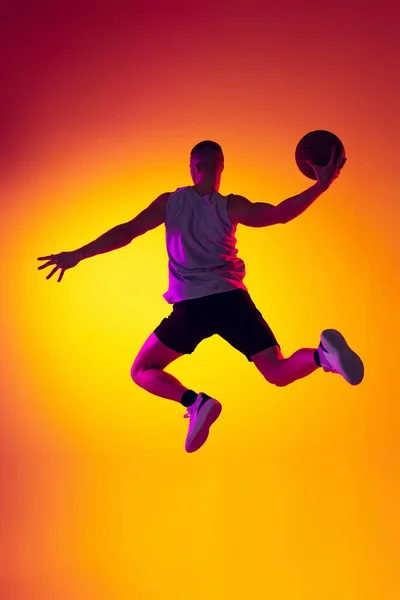 Streetballer. Jugador de baloncesto masculino, atleta saltando con pelota aislada sobre fondo amarillo anaranjado degradado en luz de neón. Deporte, diversidad, conceptos de actividad. — Foto de Stock