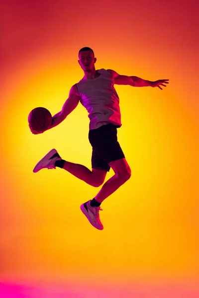 Studyjne ujęcie umięśnionego mężczyzny, trening koszykarza z piłką odizolowaną na żółtym gradientowym tle w neonowym świetle. Piękno, sport, ruch, koncepcje aktywności. — Zdjęcie stockowe