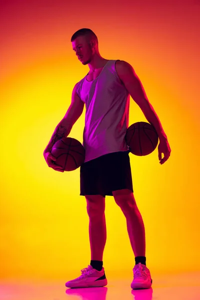 Studioaufnahme eines muskulösen Mannes, Basketballspielers, Tänzers isoliert auf gelb-violettem Hintergrund in Neonlicht. Schönheit, Sport, Bewegung, Aktivitätskonzepte. — Stockfoto