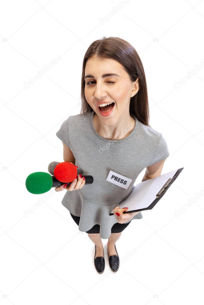 High angle view of emotional young girl, female journalist holding reporter microphone isolated on white studio background. Concept of social media, press, news, information