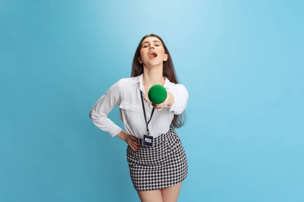 Retrato de menina bonita jovem, jornalista segurando microfone repórter isolado no fundo azul. Conceito de mídia social, imprensa, notícias, informações, emoções — Fotografia de Stock