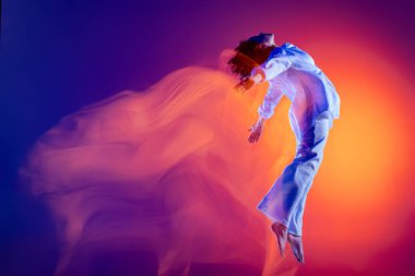 Esnek genç kız görüntüsü, beyaz kıyafetli hip-hop dansçısı, mavi arka planda izole edilmiş hip hop dansı yapan sarı neon ışığı. Gençlik kültürü, tarz ve moda, aksiyon.