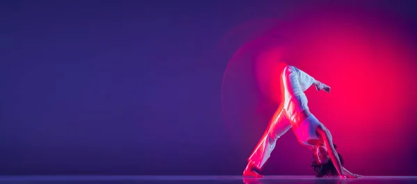 Menina bonita esportiva jovem, dançarina de hip-hop dançando hip hop isolado em fundo roxo em luz de néon rosa. Cultura juvenil, estilo e moda, ação. Folheto — Fotografia de Stock