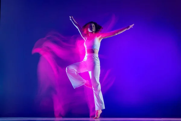 Retrato dinámico de la hermosa chica, bailarina de hip-hop en traje blanco bailando hip hop aislado sobre fondo azul en luz de neón rosa. Cultura juvenil, estilo y moda, acción. — Foto de Stock