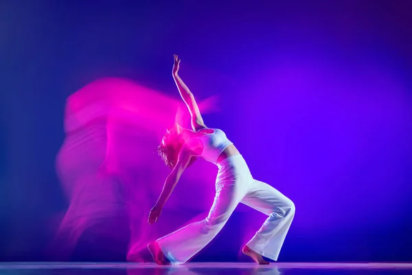 Dynamisch portret van mooi meisje, hiphop danser in witte outfit dansende hiphop geïsoleerd op blauwe achtergrond in roze neon licht. Jeugdcultuur, stijl en mode, actie. — Stockfoto